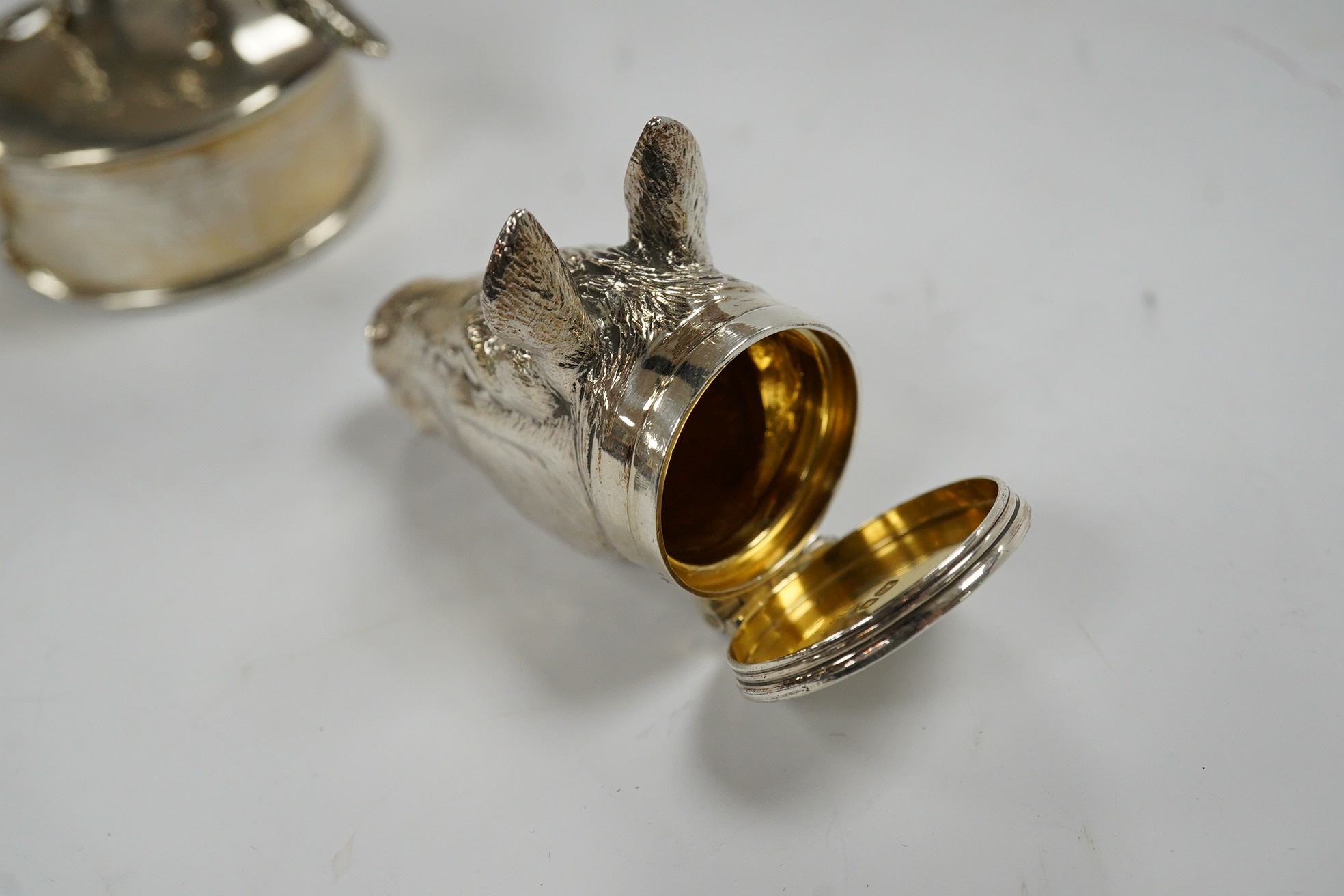 A George VI silver napkin ring modelled as a stirrup, surmounted with a fox, Birmingham, 1937, 46mm, together with a later silver horses head snuff box and a silver pill box with fox surmount. Condition - fair to good